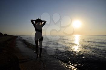 Silhouette of a girl against the sunset by the sea. The dark silhouette against the sea sunset. Girl on the beach in the evening.