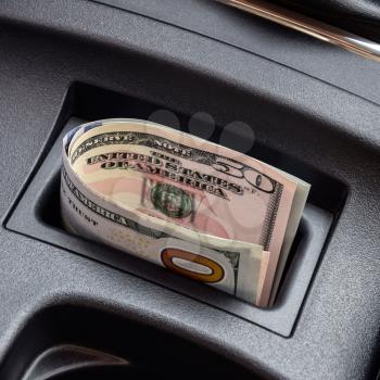 Several banknotes American dollars lie in the niche of the central console of the car. The money in the car.
