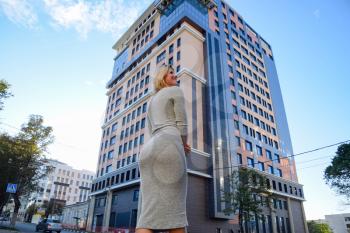 A girl with a beautiful figure in a gray dress near a tall building