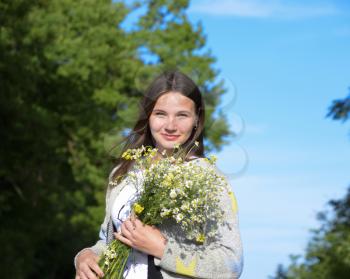 Young beautiful woman is standing in the forest with a bouquet of chamomiles.