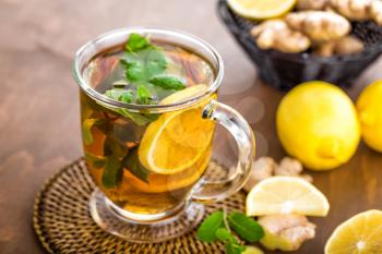 Hot herbal tea with fresh lemon, ginger and mint leaves on brown background, closeup