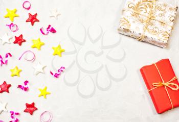 Gift with decor from stars, confetti. The composition of the present in red and gold wrapping paper and stars on a white background, birthday decorations, background