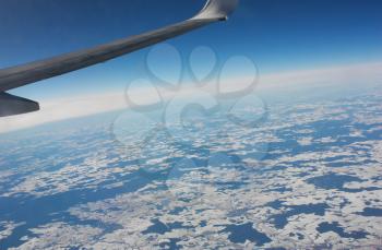 Wing aircraft in the blue sky over the ground covered with snow. View from window