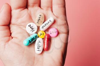 The concept of creative pills, a placebo in the hand, with joy, love, happiness, truth, power, dream on a pink background