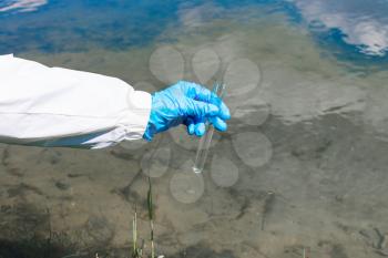 Ecologist holds a test tube with water on a background of lake, river, sea. The concept of ecology, environmental pollution