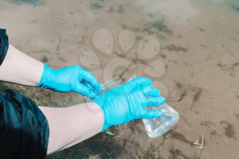 Fence, check the water sample for infections. Gloved hand with a flask and a test tube on a background of lake, river, sea. Pollution of ecology, environment
