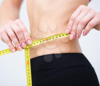 Sport, fitness and diet concept - close up of trained belly with measuring tape
