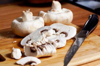 Whole and sliced white mushrooms in kitchen on wooden Board