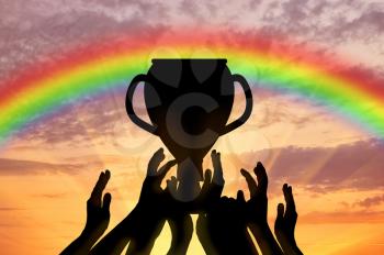 Winning the cup sport. Human hands holding the cup on the background of rainbow sunset