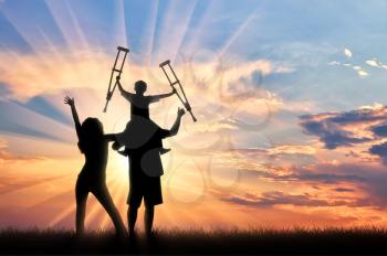 Happy parents and child invalid with crutches sits on shoulders on sunset background. Concept happy disabled and family