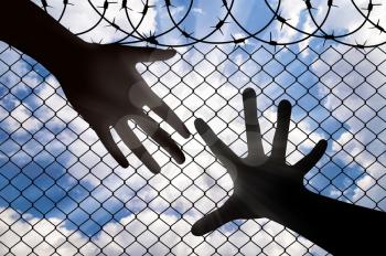 Assistance to refugees concept. A Helping Hand, reaches for the hand of a refugee, against the fence of barbed wire