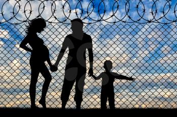 Refugees concept. Young refugee family with a child near the fence of barbed wire