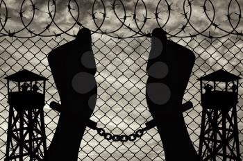 Freedom concept. Silhouette of human hands in handcuffs on a background of a watchtower and barbed wire fence