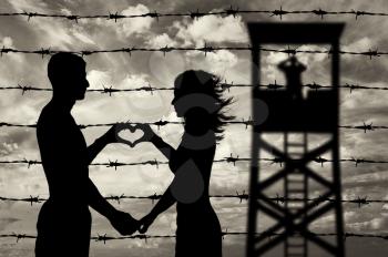 Refugees concept. Male and female refugees show hands symbol heart on the background of the fence and watchtower