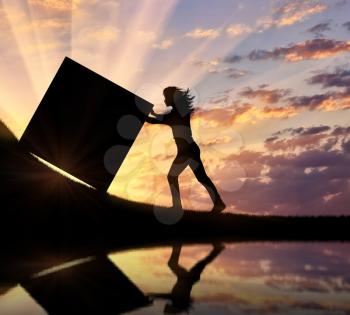Silhouette of a strong woman pushing a cube into a top and a reflection in water. Concept of effort and difficulties