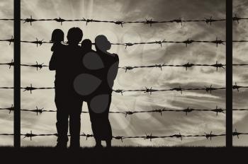 Concept of refugee. Silhouette of a family with children of refugees and fence with barbed wire