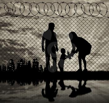 Concept of the family of refugees. Silhouette of refugee families near the fence on the border on the background of the city in the distance at sunset and reflection