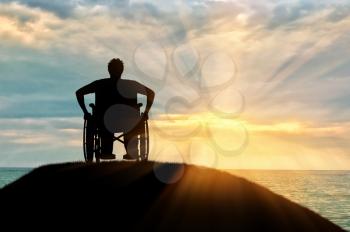 Concept of disability and old age. Silhouette of disabled person in a wheelchair on a hill against a sunset sea