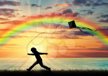 Happy child playing with kite near the sea sunset and a rainbow in sky. Concept of childhood