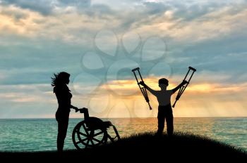 Child disabled with crutches beside wheelchair and nurse on beach on hill. Concept help.