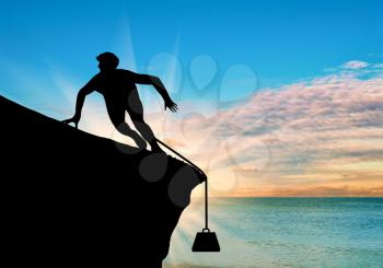 Concept of problem. Silhouette of a man on a rock and problems in the form of cargo on sea sunset background