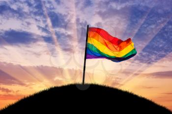 Rainbow flag on a hilltop at sunset