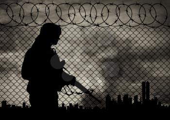 Concept of terrorism. Silhouette terrorists near the border fence in the background on the city in smoke at sunset
