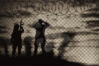 Concept of terrorism. Silhouette scouts terrorists near the border fence at sunset in smoke