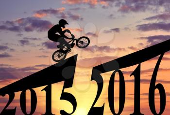 Concept of the new year. Extreme cyclist makes a jump between 2015 and 2016 years at sunset