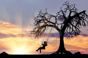 Silhouette of the girl on the swing near a tree at sunset