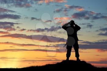 Concept of intelligence. Silhouette of soldier looking through binoculars at sunset