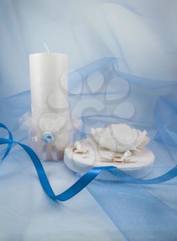  Concept of wedding accessories. Wedding rings on a pillow and a candle on a background of blue cloth