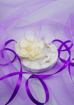 Concept of wedding accessories. Wedding rings on a pillow with a flower and violet ribbons