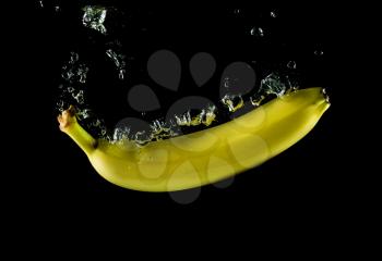 Image of banana fallen into the water on black background