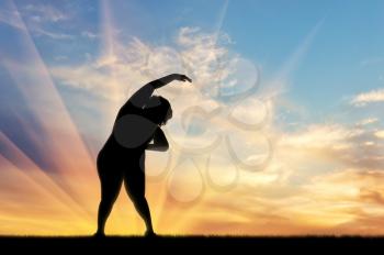 concept of fight against obesity and overweight. Silhouette of a fat woman is doing exercises at sunset