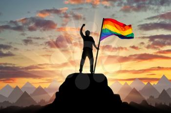 Silhouette with the gay rainbow flag on a mountain top. Concept rights gays