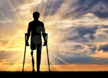 Disabled person with a prosthetic leg and crutches at sunset