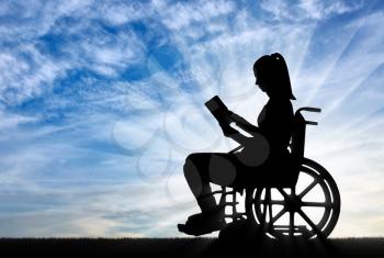 Silhouette of a disabled woman in a wheelchair reading a book in the fresh air. Concept of the way of life of people with disabilities