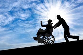 Silhouette of a disabled man in a wheelchair, having a good time with a friend, against the sky. The concept of the way of life of people with disabilities