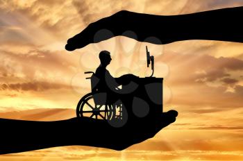 The employee is a disabled person in a wheelchair working with a computer at the table, he is in the hands of man. The concept of protection of the rights of persons with disabilities to get a job