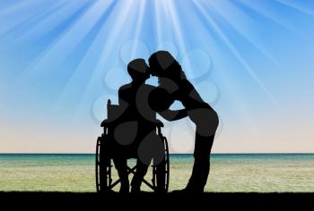 Silhouette of a disabled man in a wheelchair and his wife who is kissing by the sea. The concept of caring and supporting disabled people