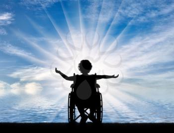 Silhouette of a happy disabled child girl sitting in a wheelchair at the seaside. Concept of happy children with disabilities