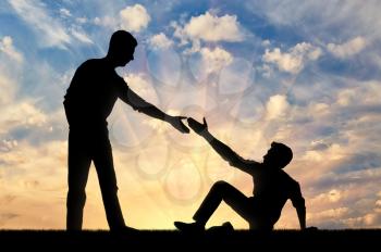 Silhouette of a man giving a helping hand to another man who fell to the ground. The concept of a helping hand