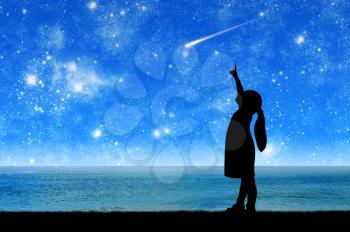 Silhouette, little girl a child standing by the sea looking at the starry sky and pointing a finger at the flying meteorite. Conceptual image of children's dreams and fantasies