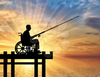 Silhouette of a disabled man in a wheelchair with a fishing rod in his hand fishing near the water. Concept of leisure and leisure of people with disabilities