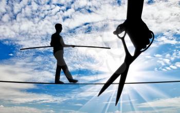 Silhouette of a businessman walking on a tightrope balances and a hand with scissors intends to cut the rope. Concept of danger and risks in business