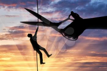 Silhouette of a businessman climbs on a tightrope and a hand with scissors intends to cut a rope. Concept of risks in business
