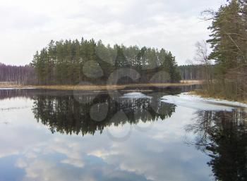 River landscape in early spring with clouds reflected in the water and ice floes.
