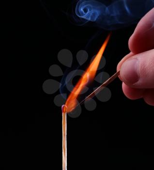 Ignition of a match, with smoke on dark background. Hand holding burning match stick