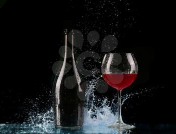 Glass and bottle of red wine splash on black
